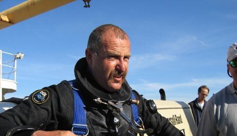 A Deep Sea Diver in a diving suit standing next to a boat.
