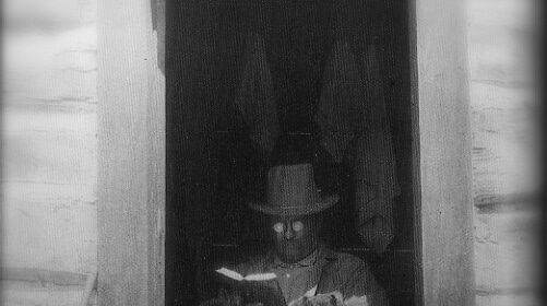 A man sitting in a doorway speed reading a book.