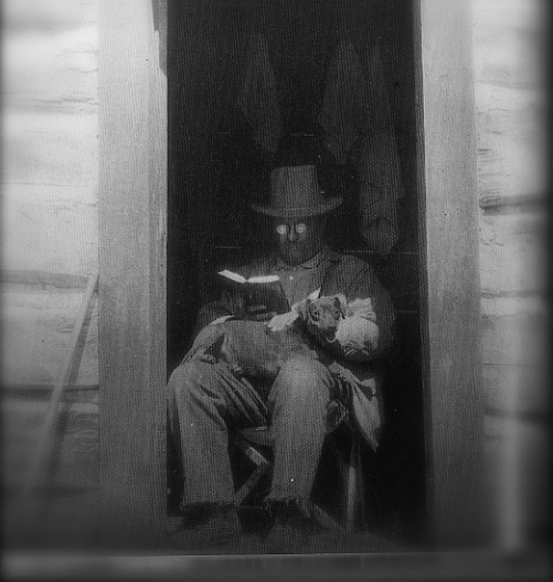 A man sitting in a doorway speed reading a book.