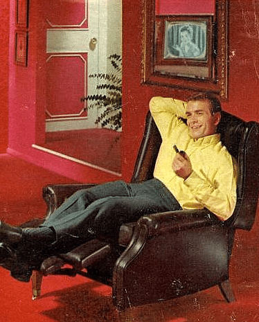 Man lying on sofa while smiling and smoking pipe in his hand.