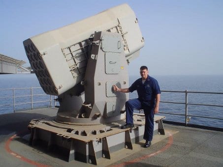 A Navy Sailor standing next to a missile on the deck of a ship.