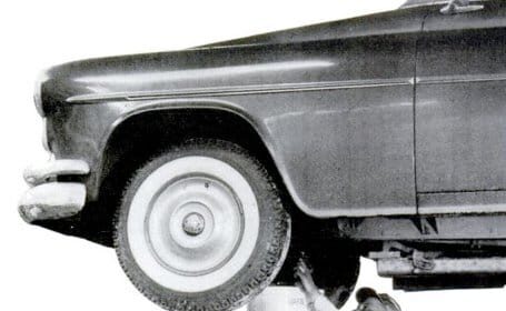 An old photo of a man changing motor oil on a car.