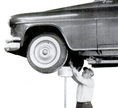 An old photo of a man changing motor oil on a car.