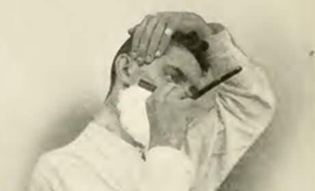 An old photo capturing a man gracefully shaving his head with a straight razor.