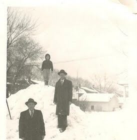 Three men showcasing their manliness, confidently standing on top of a pile of snow.