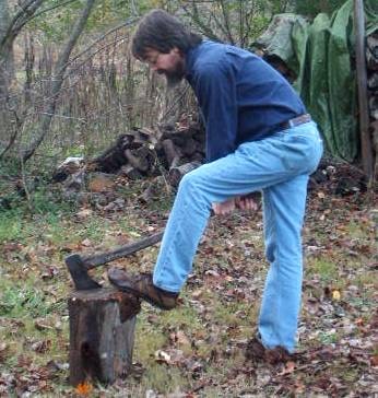 Man removing axe from log while placing his leg on log.