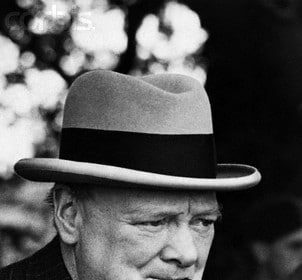 A man in a suit and hat choosing a good cigar to smoke.