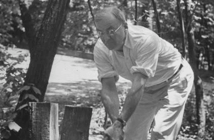 An old black and white photo capturing a man splitting firewood by cutting down a tree.