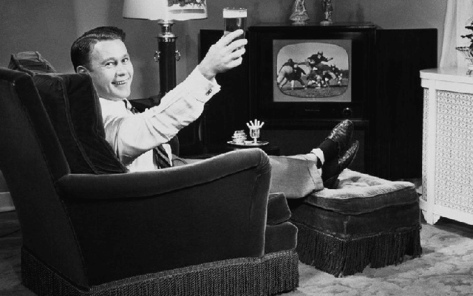 Formal man lying on chairand cheering beer while watching tv.