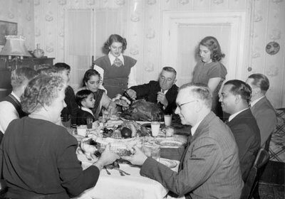 A group of people sitting around a table, enjoying Thanksgiving dinner with cornbread stuffing.