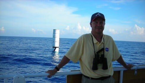 A rocket scientist standing on the deck of a boat in the ocean, contemplating his job.