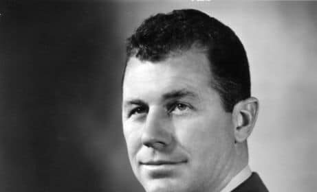 A black and white photo of a manly man in uniform.