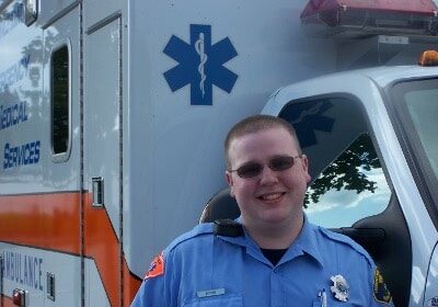 An EMT is standing in front of an ambulance.
