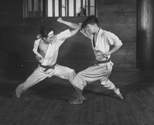 Two men getting started in martial arts, practicing karate in a room.