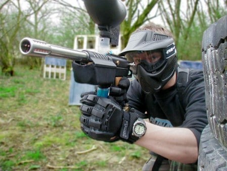 Man wearing helmet and playing paintball in an open area.