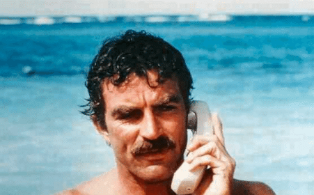 A shirtless man with a chest talking on a cell phone on the beach.