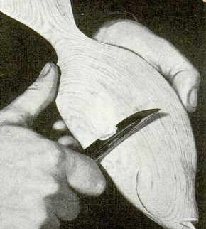 Man whittling fish out of wood with pocket knife.