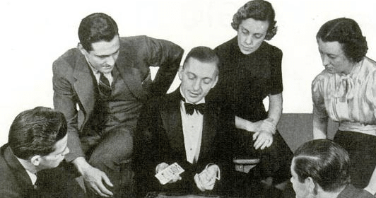 A group of people sitting around a table playing cards while a magician amazes your friends with props.