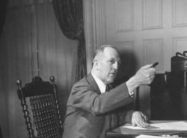 An old photo of a man showing leadership while sitting at a desk.