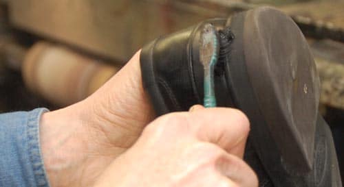 Hombre aplicando betún para zapatos de cuero con un cepillo de dientes.