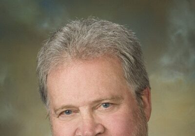 A man in a purple shirt, who is also a federal prosecutor, with a beard.