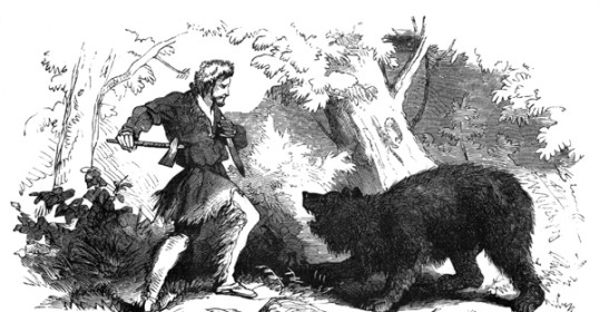 A man stands next to a bear in the woods during a Wild West adventure.