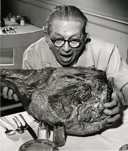 Vintage man eating lamb roast in kitchen.