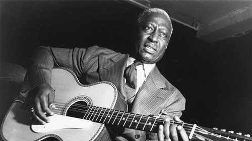 An acoustic guitar player strums a melody in this black and white photo.