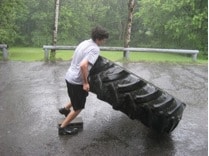 Man lifting truck tire on road.