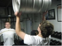 A man training with lifting kegs at gym.