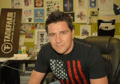 A man sitting at a desk wearing an American flag t-shirt, which he designed himself.