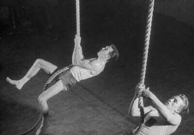 Two men engaging in guide training on thick ropes in a gym.