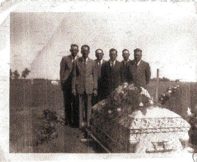 A group of men howling next to a casket as they plan a funeral.