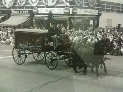 Funeral carried on horses along with several people watching it.