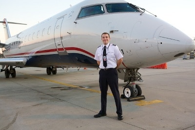 An airline pilot in uniform standing in front of an airplane.