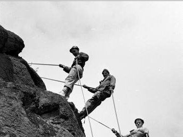 A group of people displaying manliness as they courageously climb up a rock.