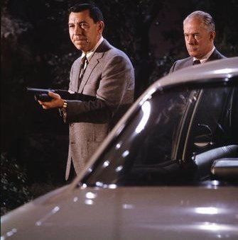 Two men in classic suits standing next to a car.