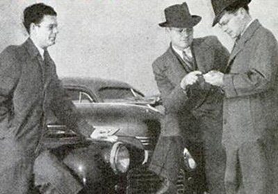 Three men negotiate next to a used car.