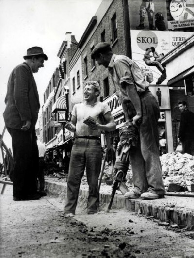 Vintage men talking in street and one man doing drilling on the ground.