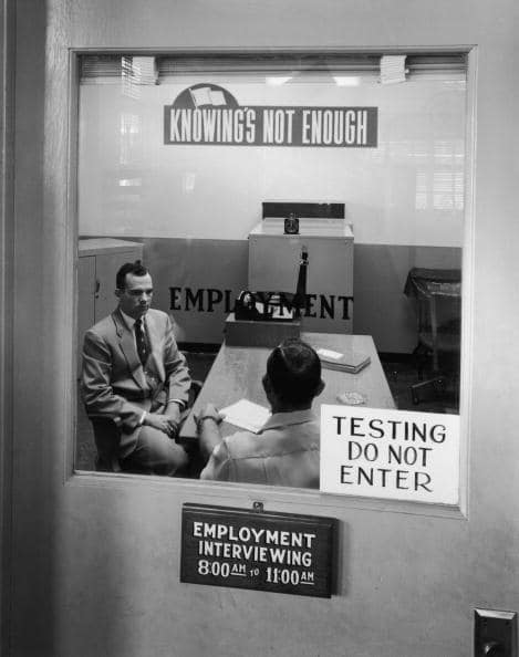 A man in a suit prepares for a behavioral job interview at an office desk.