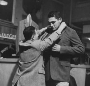 A man is assisting another man in a style transition by helping him dress.