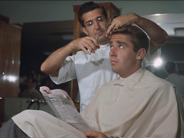 Man looking towards barber for hair cut and a newspaper in his hands.