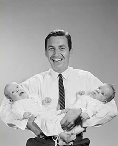 A black and white photo of a man, guide for fathers, holding two babies.