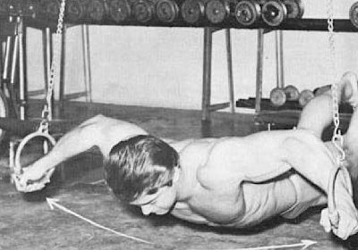 A vintage photo capturing a man performing rigorous ring exercises, showcasing his strength and mastery of bodyweight training.