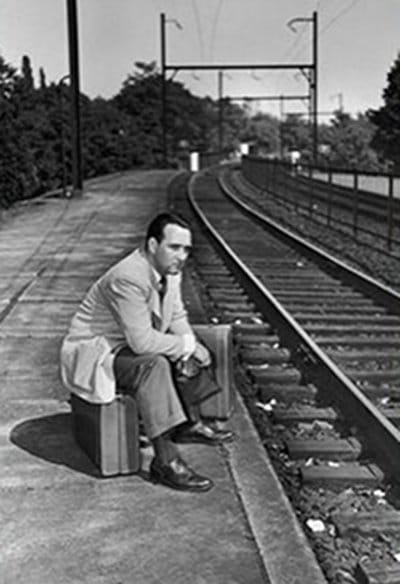 Vintage man in suit sitting alone at railroad tracks.