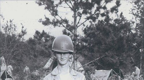 Easy Company soldier Robert Rader standing in front of a tent surrounded by fellow men.