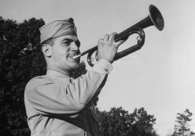 An early riser in uniform playing a trumpet as the sun rises.