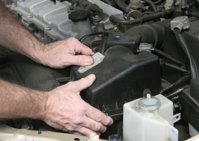 Man changing air filter box under car hood.