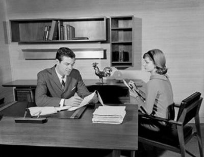 Vintage boss and secretary taking notes at desk.