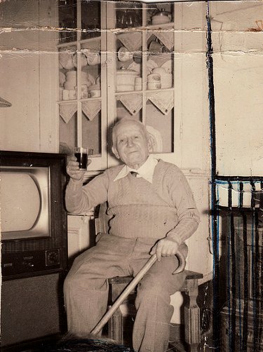 Vintage older man sitting on chair and holding glass in hand.